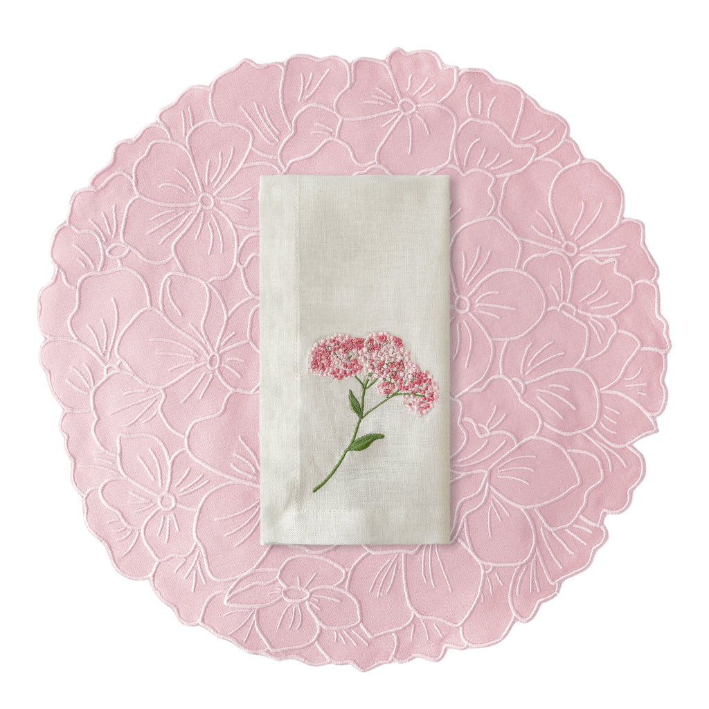Set de mantelería con individuales en forma de flor hortensia en rosa, con servilletas de lino blanco con bordado de flor rosa, marca Zash