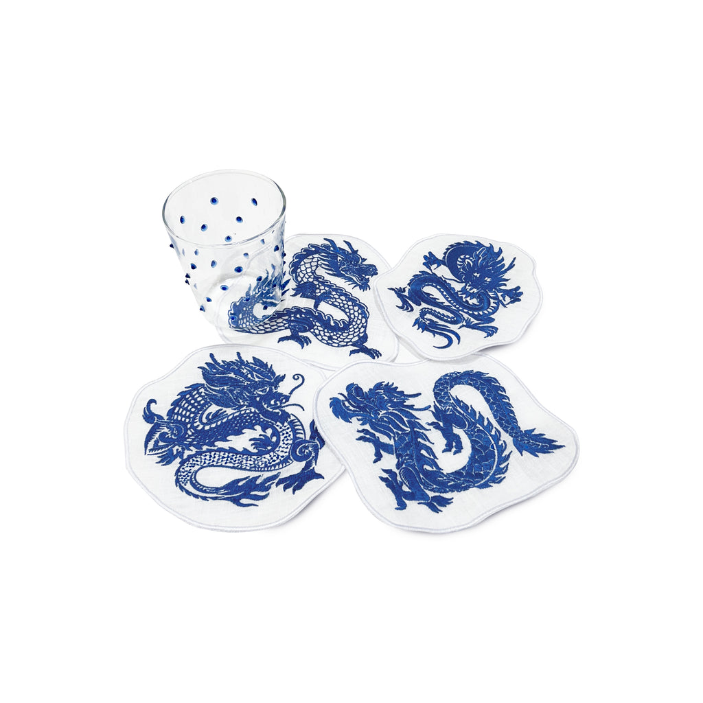 Set de servilletas cocteleras de lino blanco con dragones bordadas en azul con vasos con puntitos azules, marca Zash
