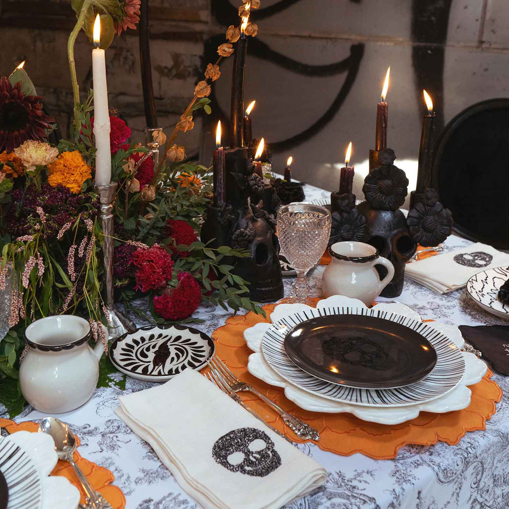 OFRENDA ZASHPACK: Set de Individuales en Forma de Cempasúchil en Loneta Naranja, Servilletas en Lino con Calaca Bordada en Negro, Platos Trinche de Rayas Negras y Platos para Ensalada Negros con Calaca. Set para 4 personas