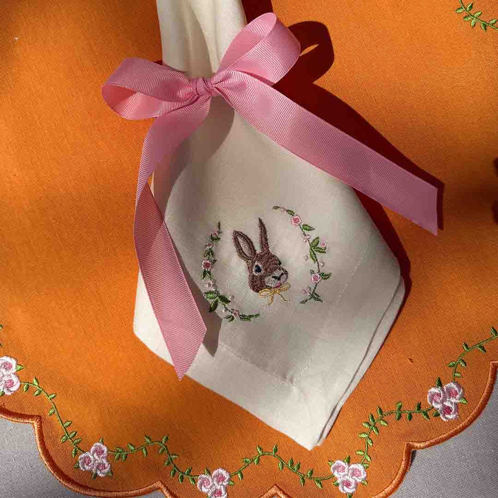 Mantelería Easter con Individual Pily en Algodón Naranja con Bordado de Florecitas y Servilleta Easter en Lino Ivory con Bordado de Conejo . Set de 4