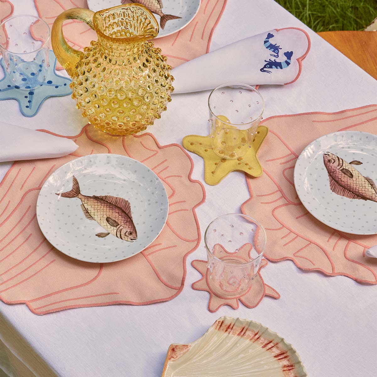 Mesa de playa o para servir mariscos, con mantelería en forma de coral rosa y platos con pez