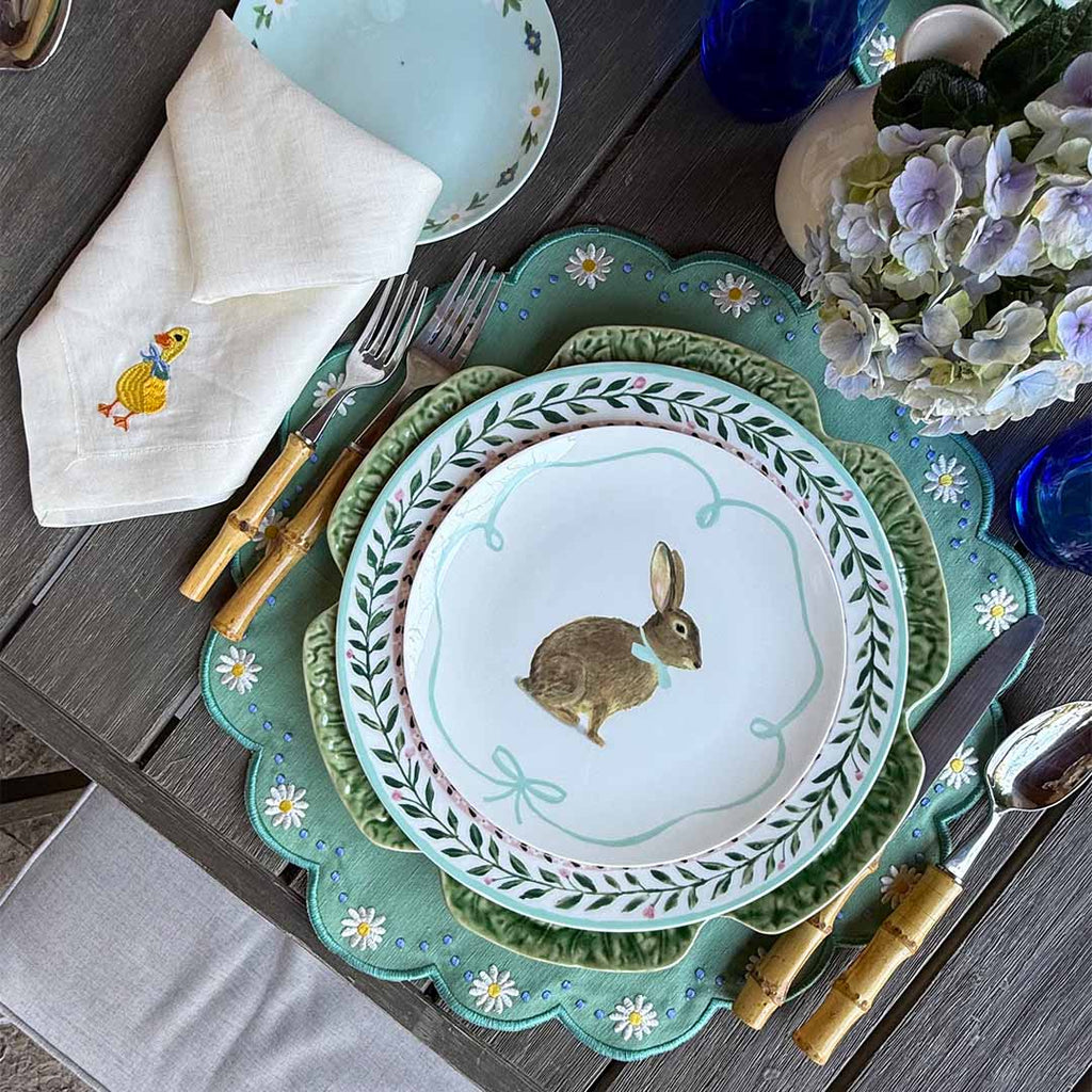 THE DUCKLING ZASHPACK: Set con 4 Servilletas Easter en Lino Ivory con Bordado de Pato, 4 Individuales Pily en Algodón Verde con Bordado de Margaritas y 4 Platos Trinche con Borde de Flores.