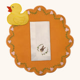 Mantelería Easter con Individual Pily en Algodón Naranja con Bordado de Florecitas, Servilleta Easter en Lino Ivory con Bordado de Conejo y Coctelera en Algodón Amarillo con Bordado de Pato. Set de 4