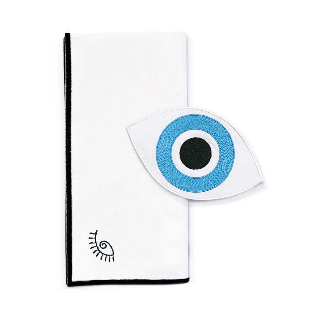 Set de mantelería con servilletas cocteleras en forma de ojo de la suerte, y servilleta de lino con orilla bordada en negro y ojito. Marca Zash