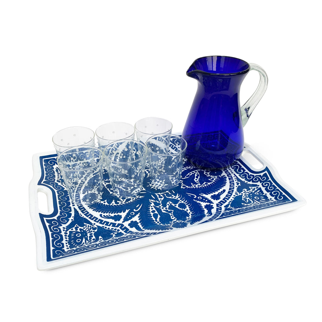 Charola artesanal de madera de Olinalá azul con blanco, con vasos tumbler de vidrio con puntitos blancos, y jarra de vidrio soplado en azul