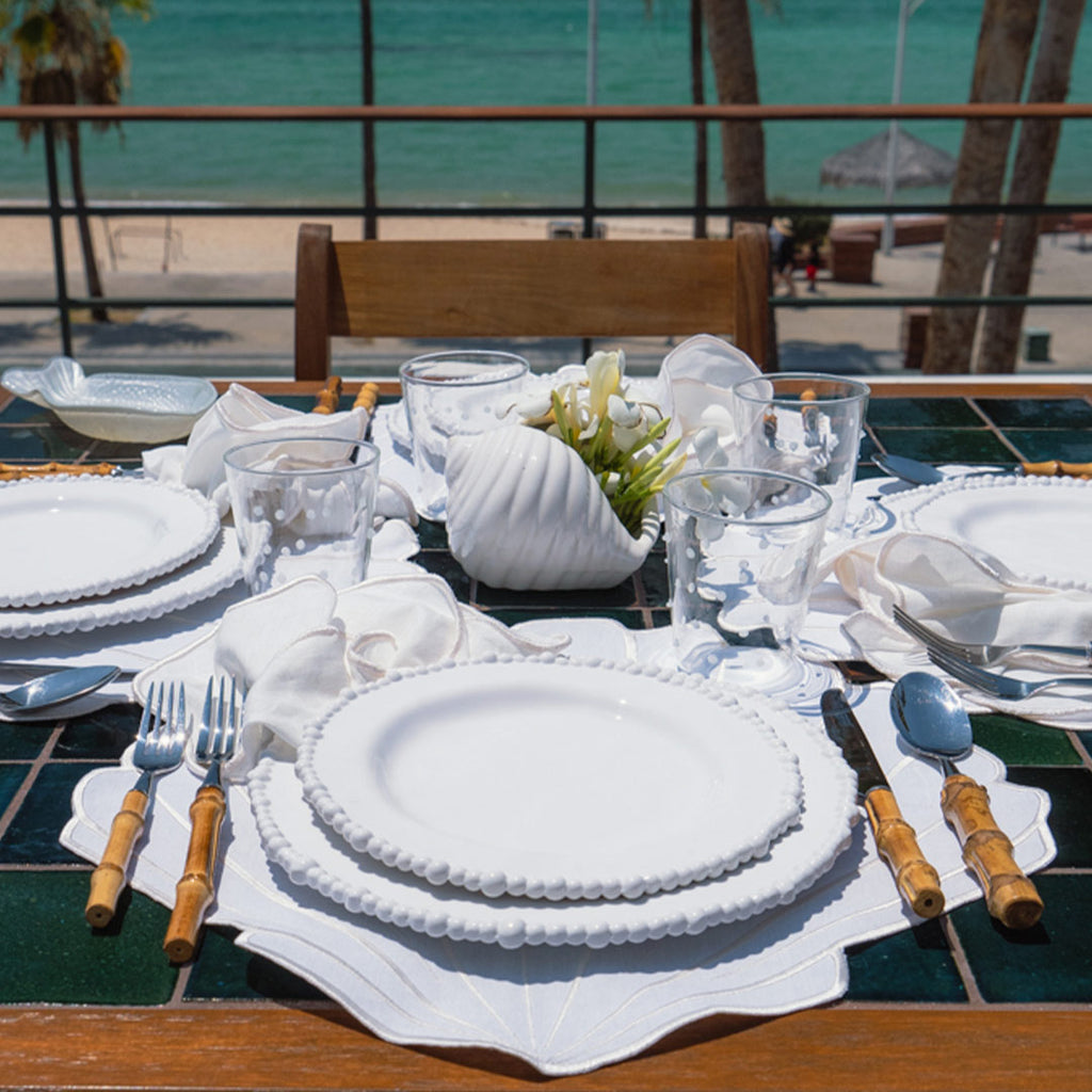 Set Mantelería Concha en Ivory: 4 Individuales en Forma de Concha con 4 Servilletas con Orilla Bordada en Ivory.