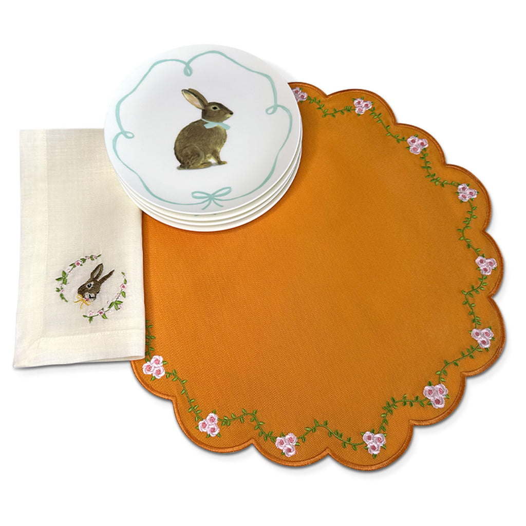 Set de mesa con Individuales Pily en algodón naranja y bordado de flores, servilleta de lino ivory con conejito bordado, y platos de ensalada con ilustración de conejo, marca Zash